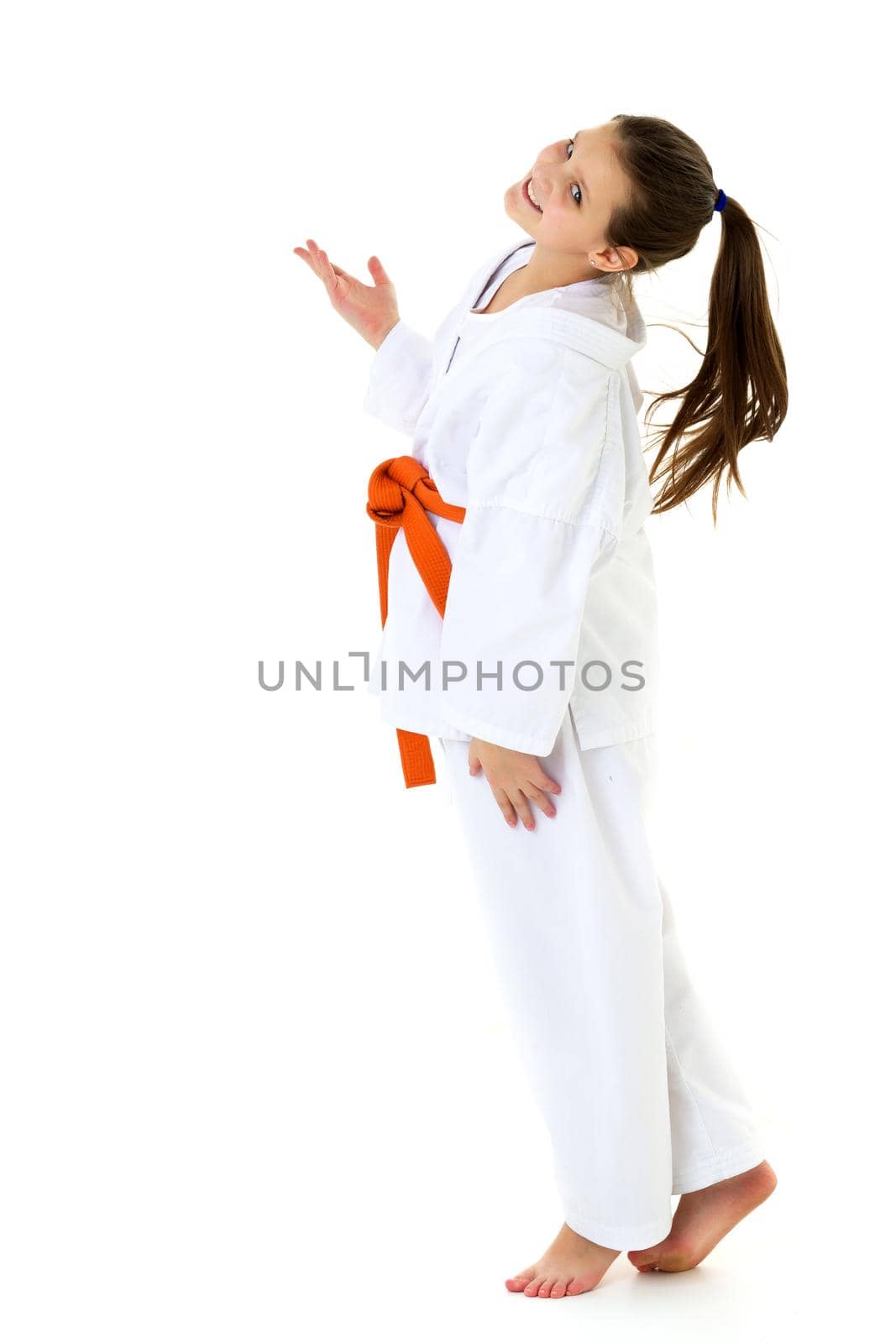 A teenage girl dressed in a kimono with an orange sash. Cheerful beautiful long-haired girl dressed in sportswear, on an isolated white background. Healthy lifestyle, sport and fitness concept