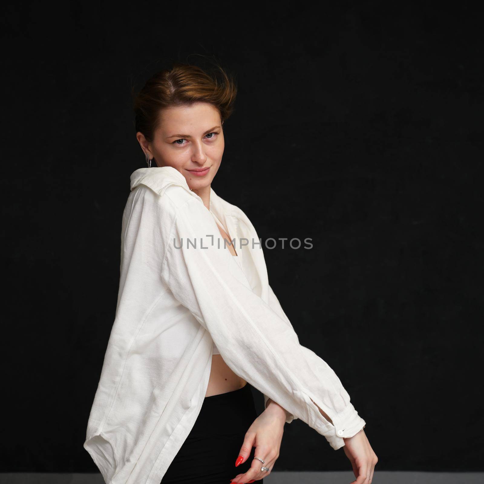 Portrait of smiling girl in light clothes posing in studio on black background