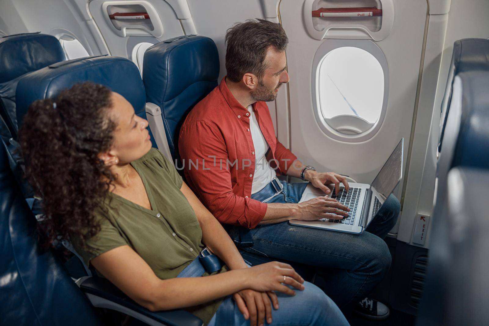 Caucasian man looking out the window, using laptop computer while sitting on the airplane. Transportation concept