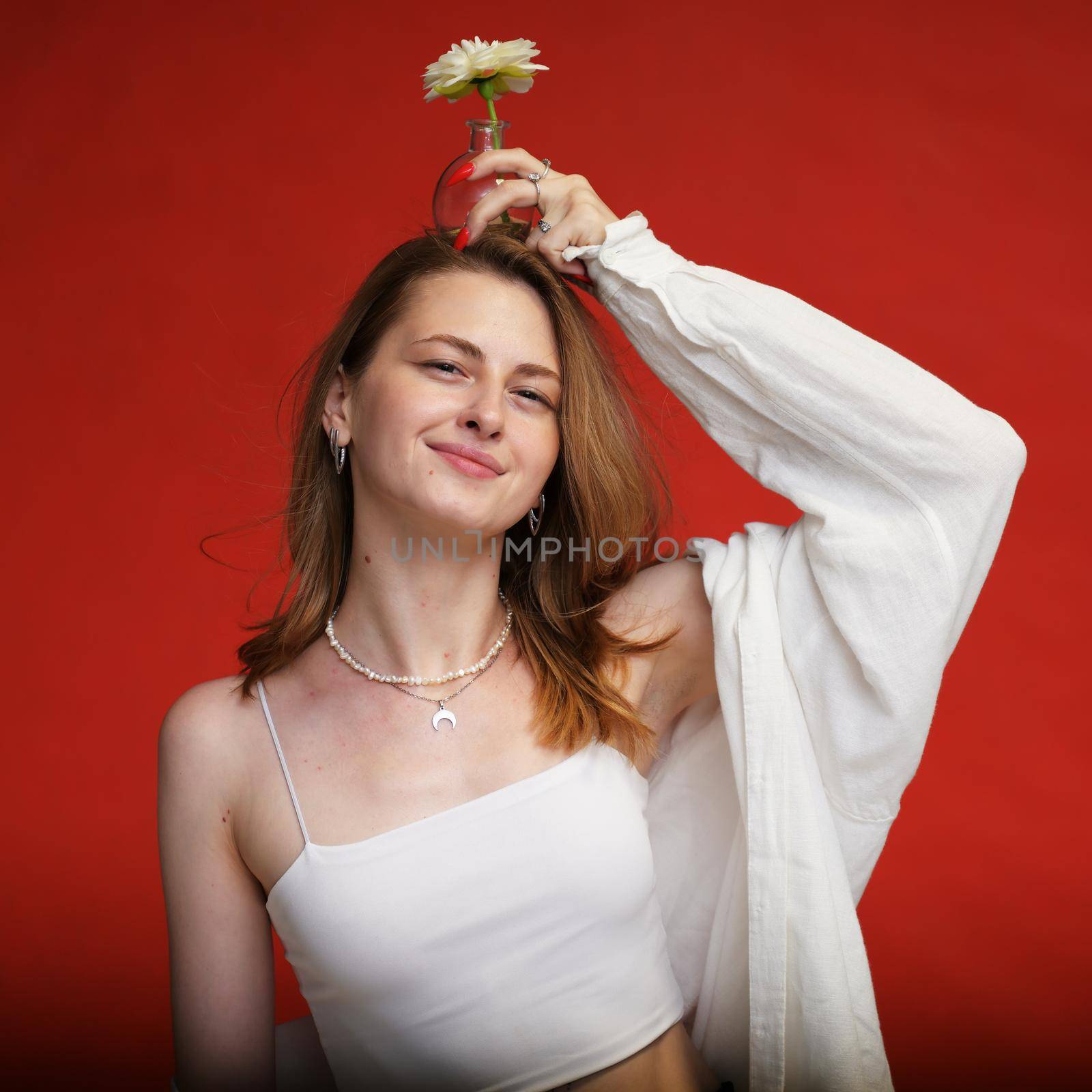Caucasian smiling girl wearing white clothes posing with flower in studio on red background by chichaevstudio