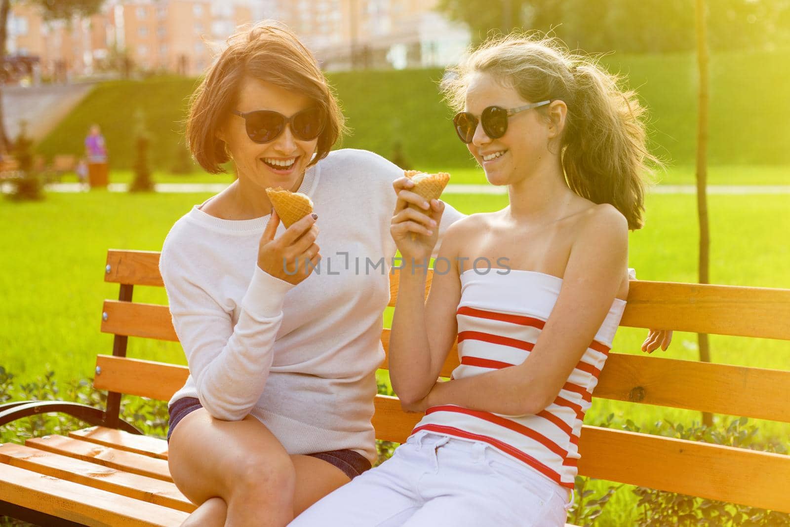 Holiday with the family. Happy young mother and cute daughter of a teenager in a city park eating ice cream, talking and laughing