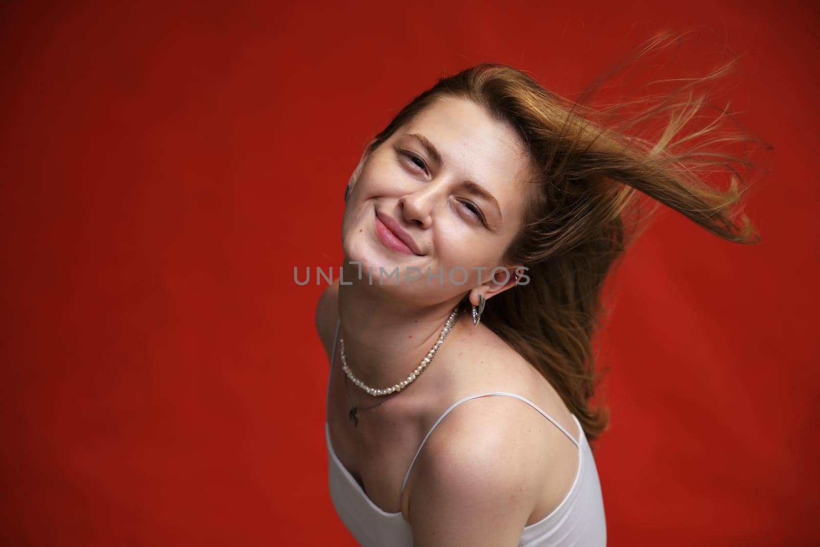 face portrait of happy caucasian girl with fluttering hair in light clothes on red background by chichaevstudio