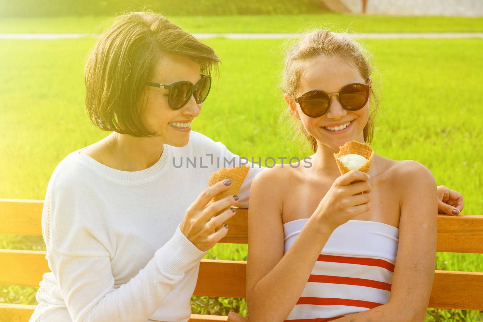 Holiday with the family. Happy young mother and cute daughter of a teenager in a city park eating ice cream, talking and laughing