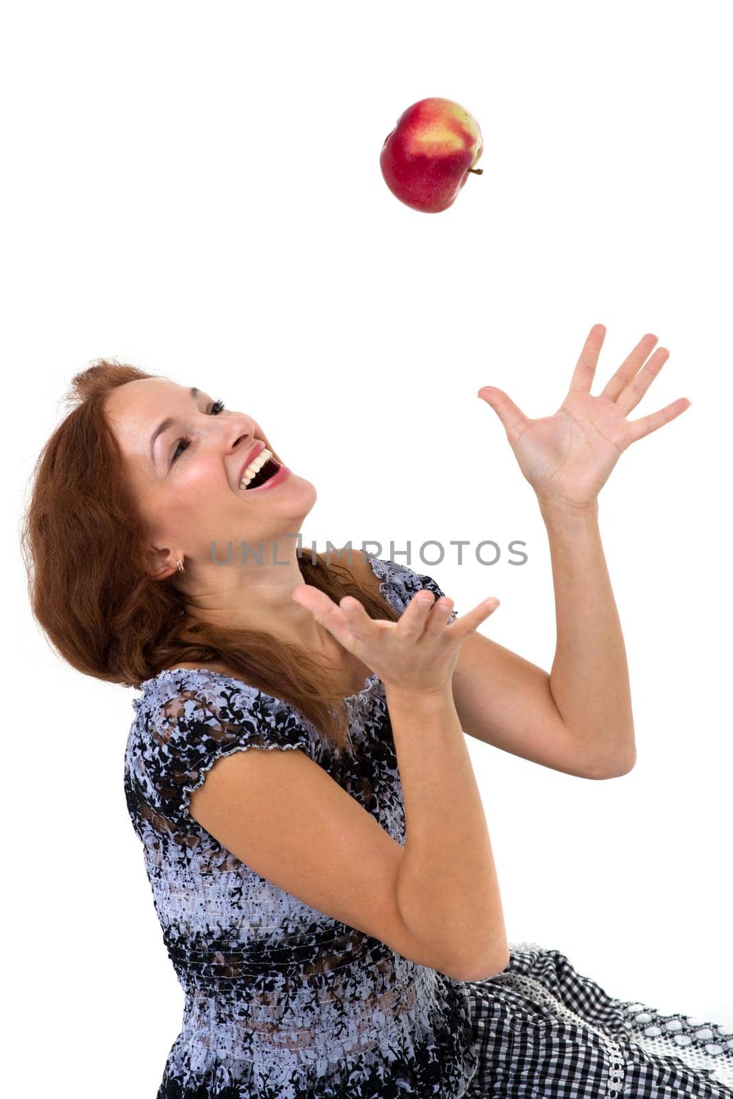 Smiling happy girl throwing up red apple in the air. Portrait of joyful girl in summer dress sitting on isolated white background. Healthy eating and diet concept