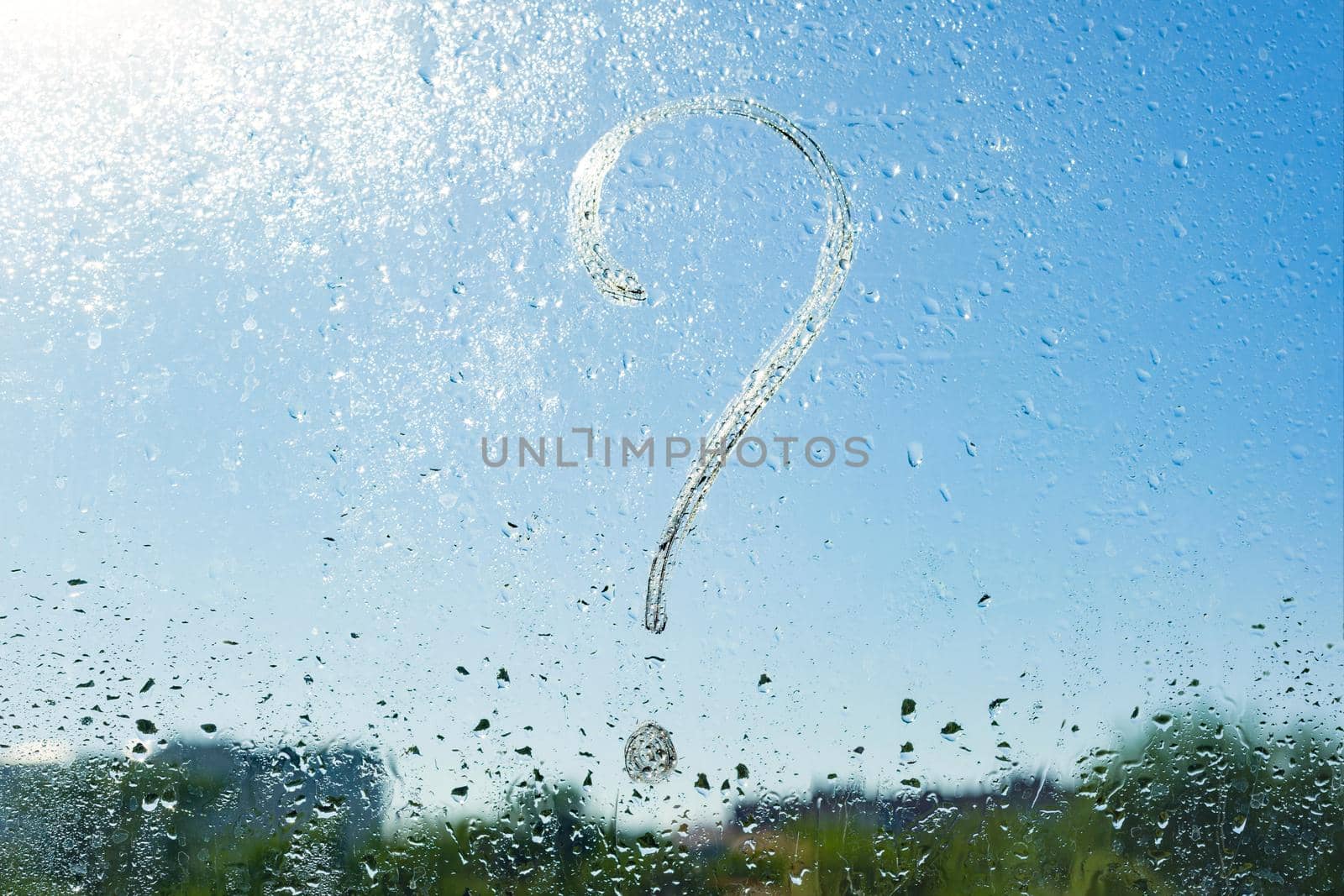 Handwritten question mark on rainy window. Background drop of water on the glass, blue sky, sun.