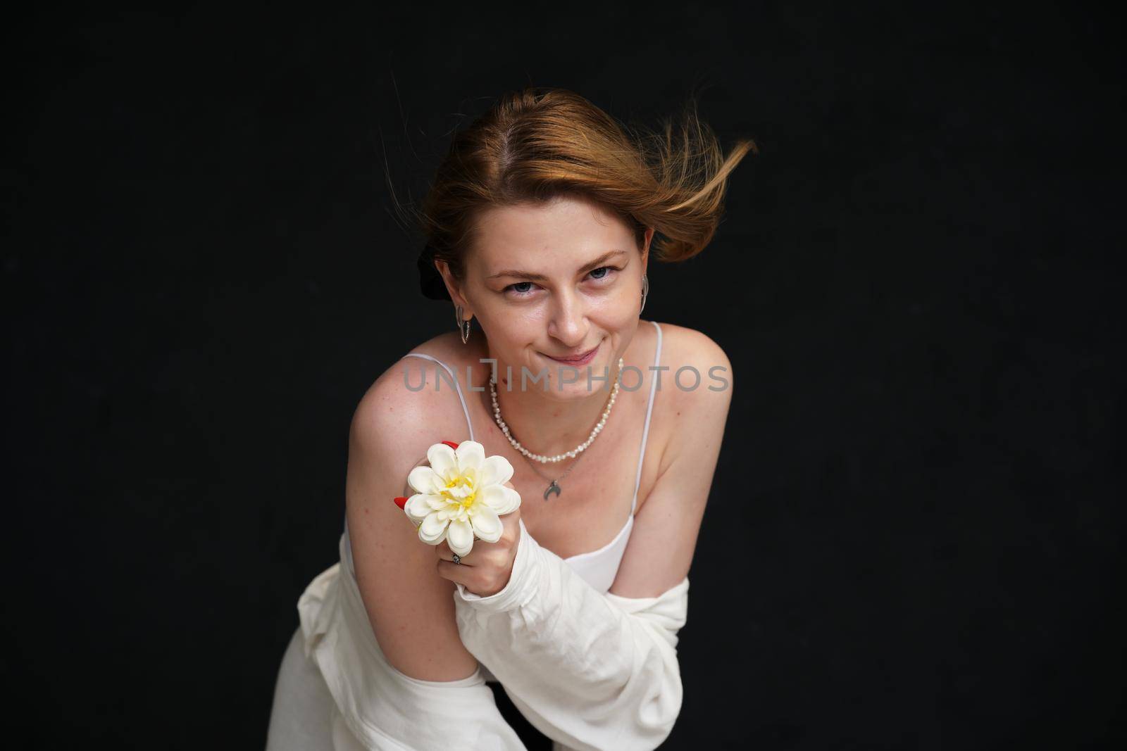 happy model in white shirt posing with flower with smile on black background