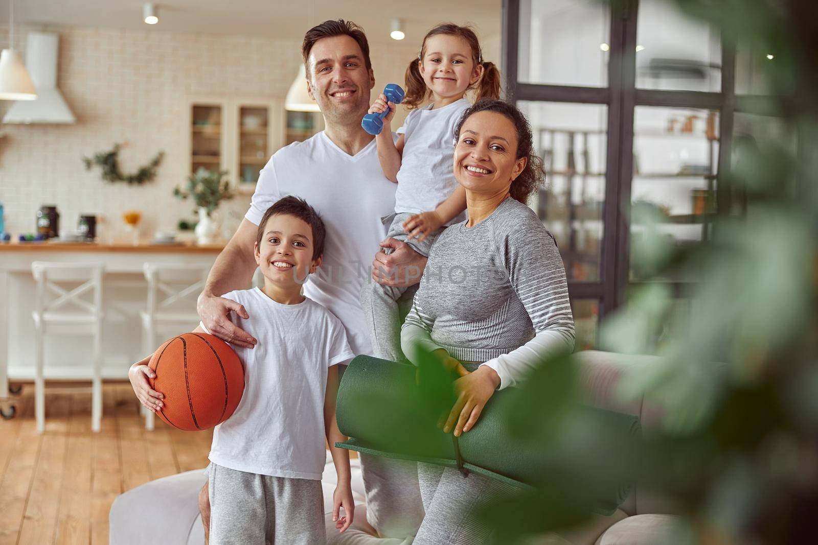 Full length portrait of smiing mom and dad with children holding equipment for workout at home