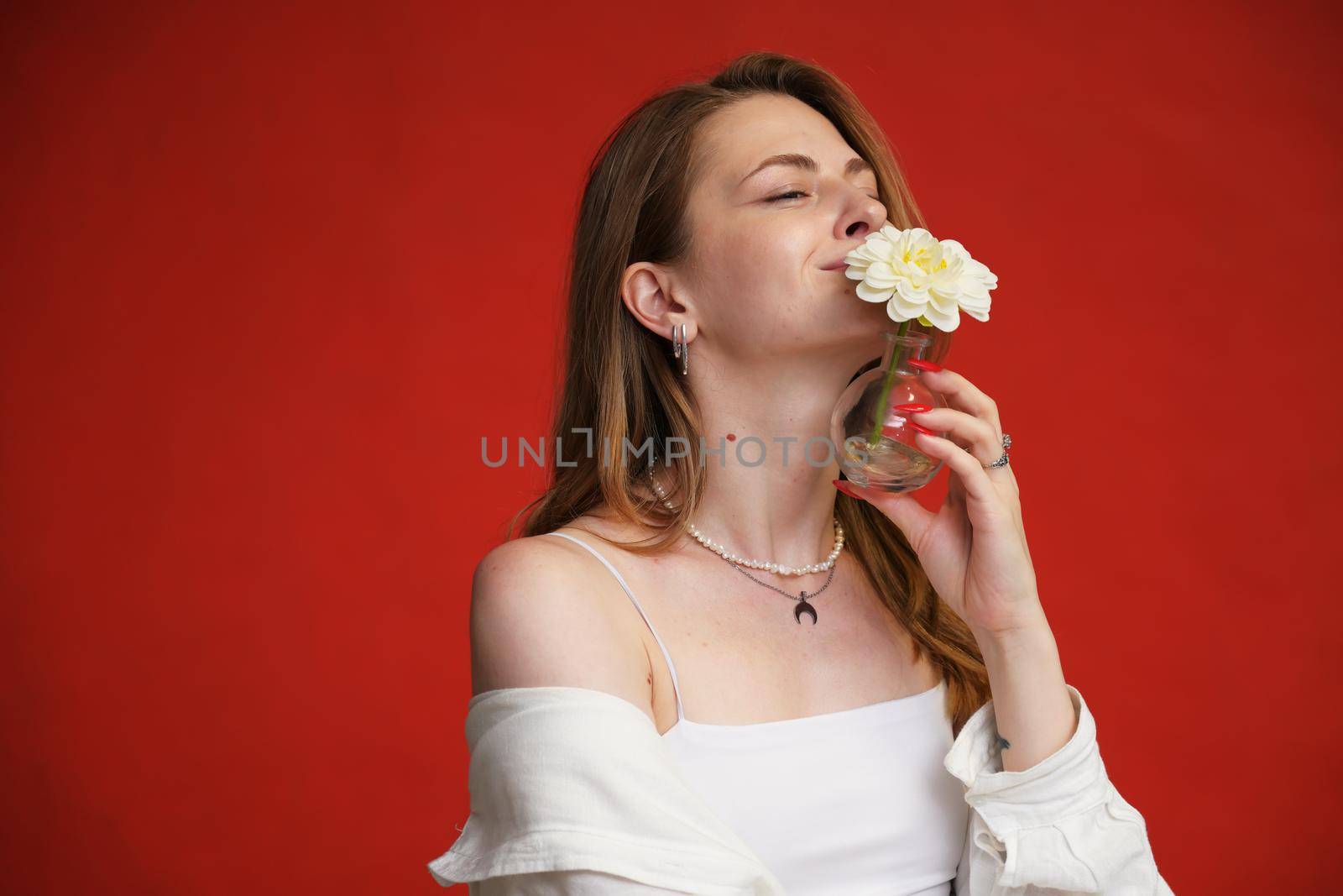 Young model in white shirt posing with flower with smile on red background by chichaevstudio