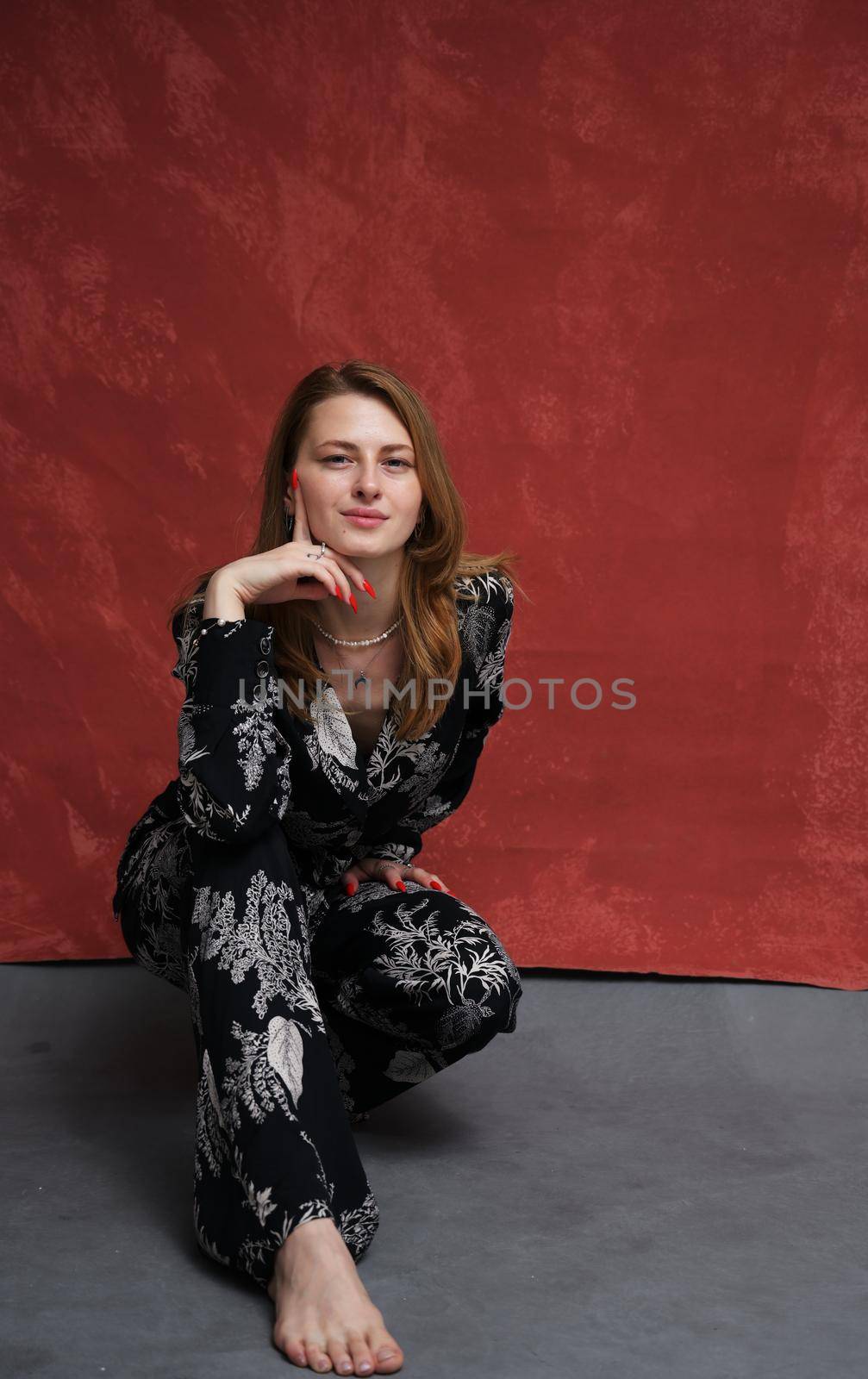 vertical view of caucasian model girl in squat posing in studio on dark red and gray background