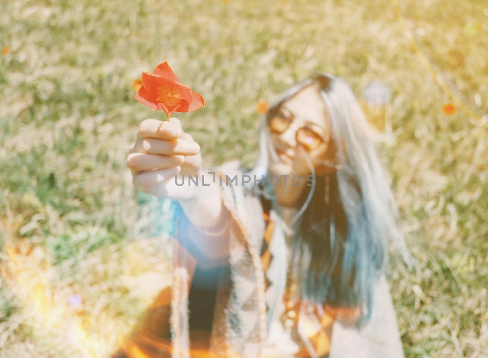 Beautiful young woman boho style gives a red tulip outdoor on sunny day.
