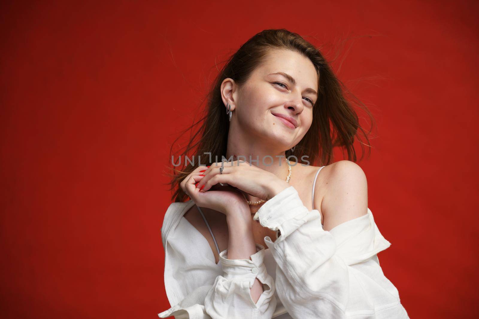 portrait of a cute smiling girl in a white blouse in a studio on a red background by chichaevstudio