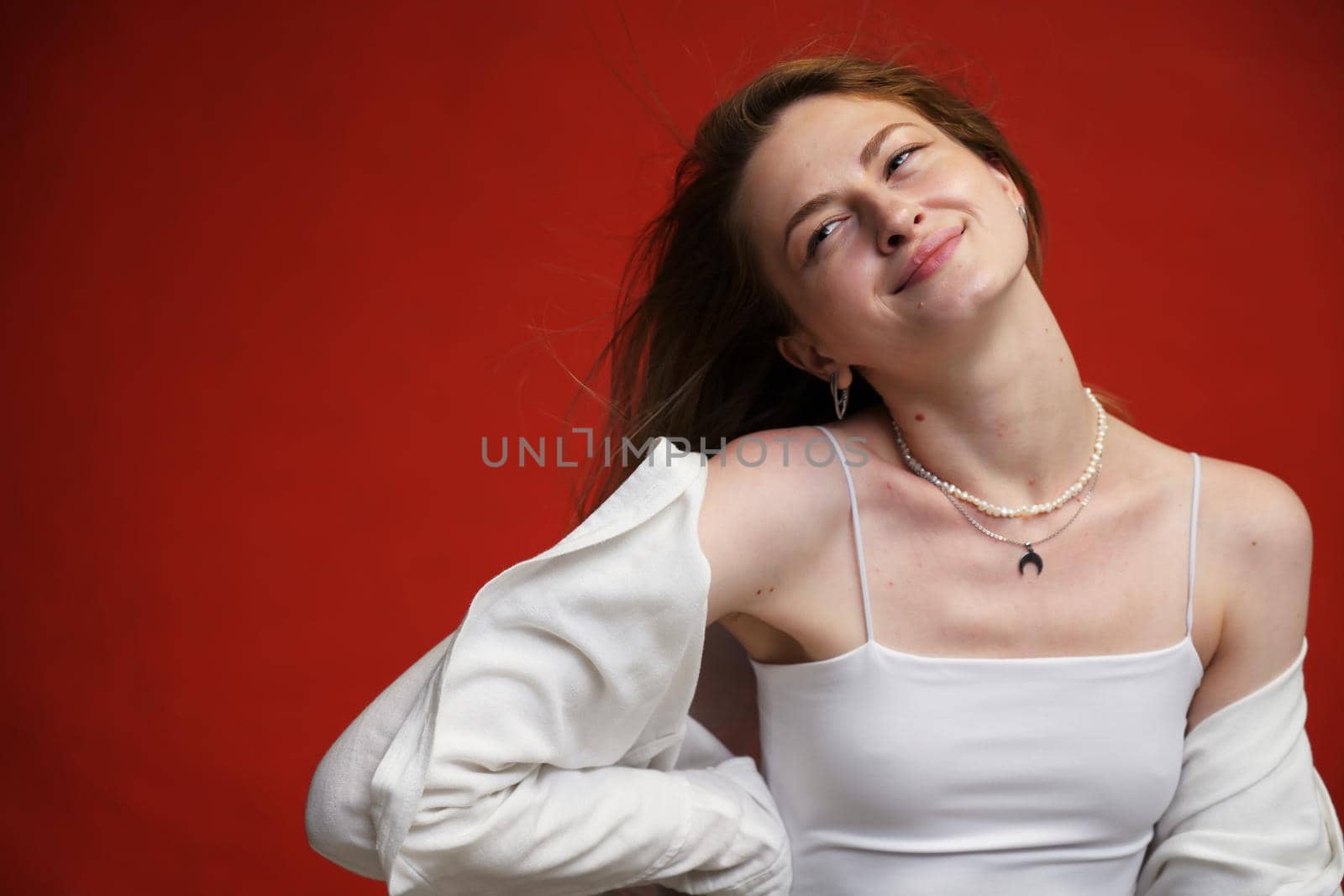 smiling caucasian girl with fluttering hair posing with pleasure in light clothes on red background