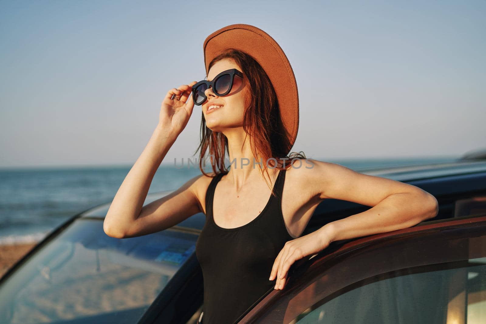 cheerful woman in sunglasses and a hat on the ocean near the car. High quality photo