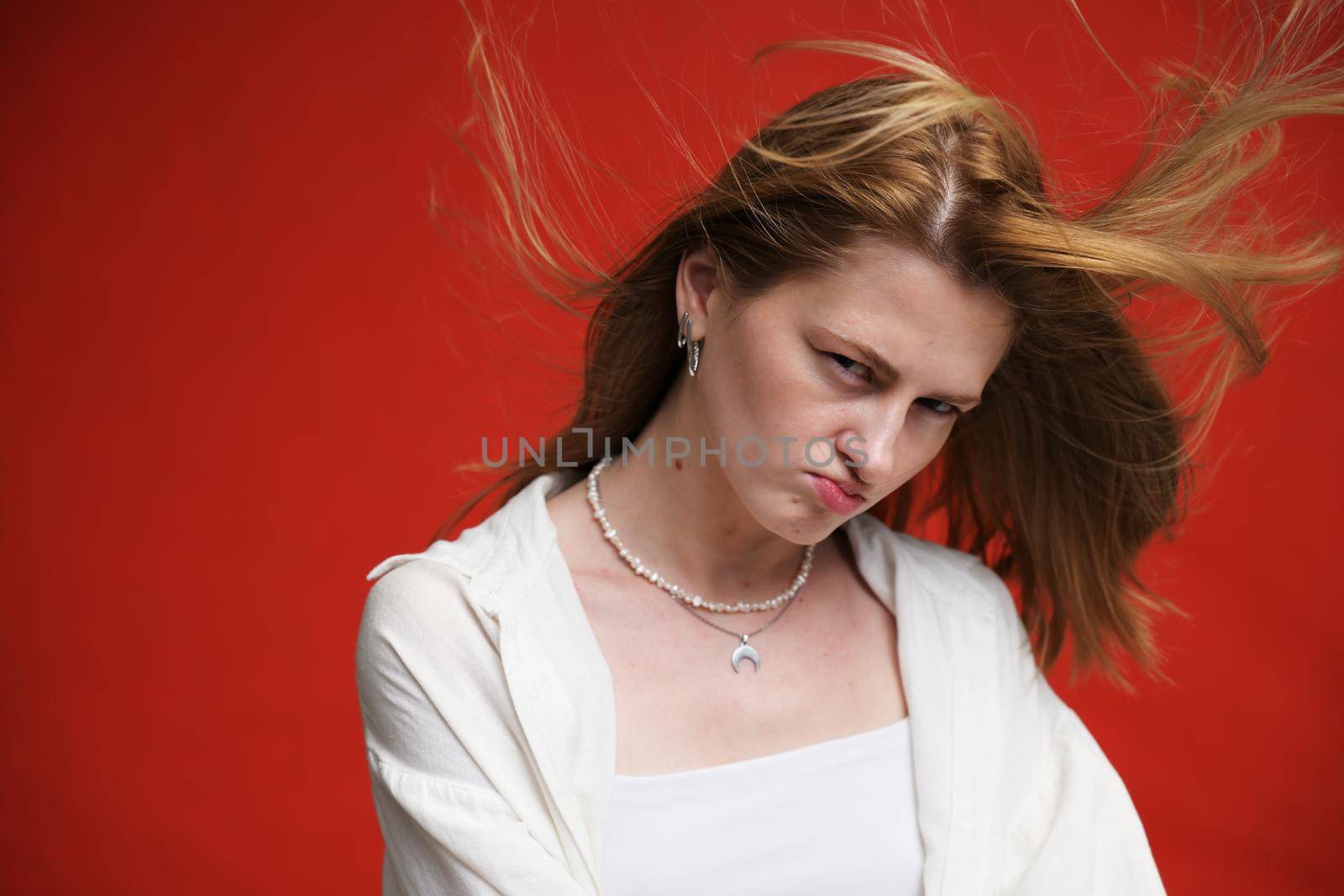 face portrait of a displeased caucasian girl in light clothes on a red background by chichaevstudio
