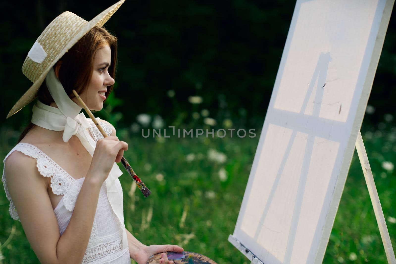 Woman in white dress paints a picture on nature easel. High quality photo