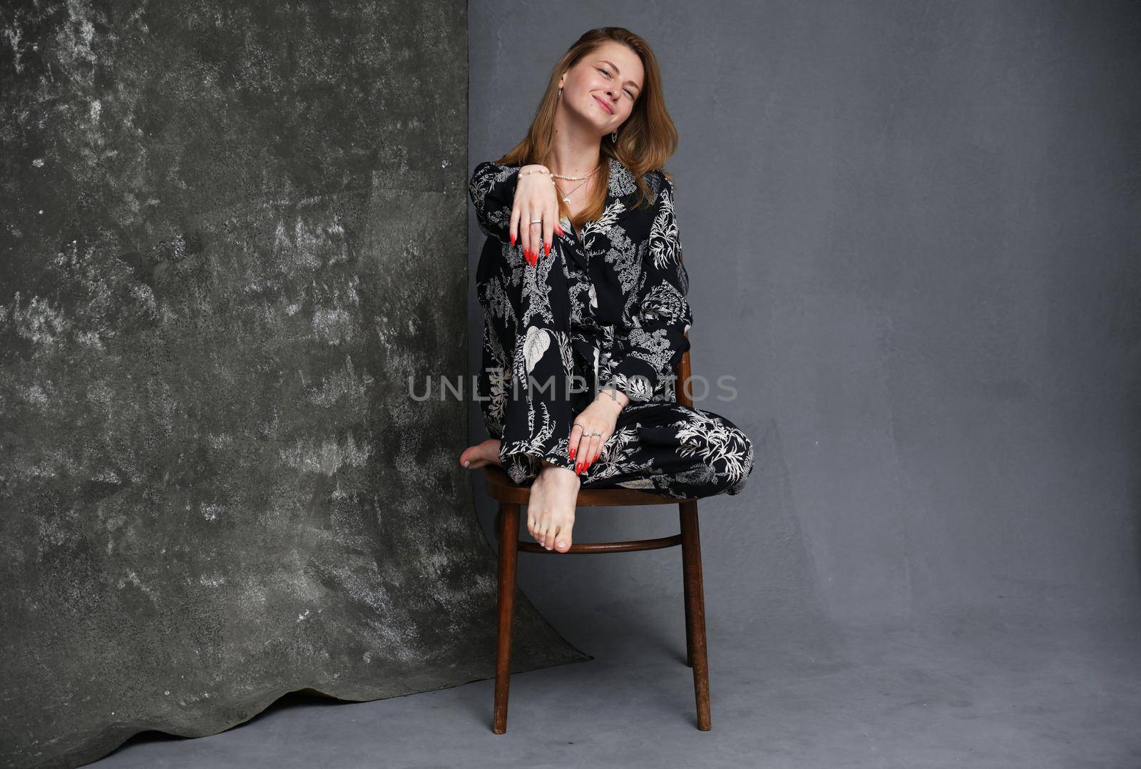 Photo in full growth caucasian girl in dark clothes sits on a chair in the studio on a gray background