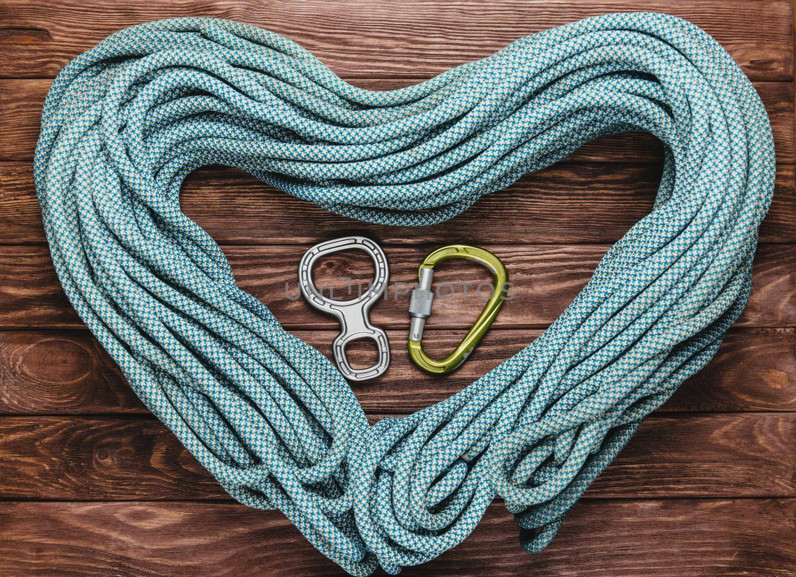 Rope for climbing in the shape of a heart with carbine and figure eight on wooden background, top view.