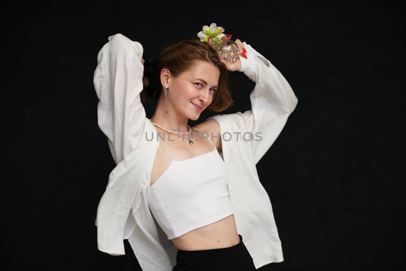 cute smiling caucasian girl with fluttering hair posing with a flower in her hand in light clothes on a black background
