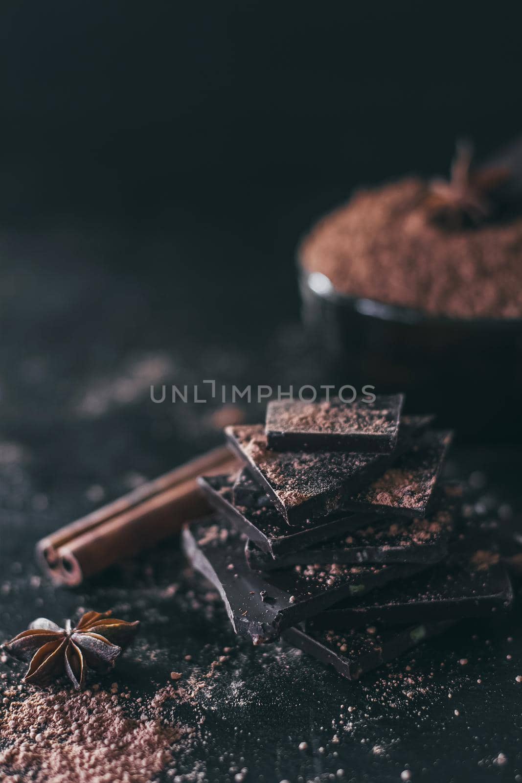 Chocolate bar pieces with cocoa powder on dark background, cope space.