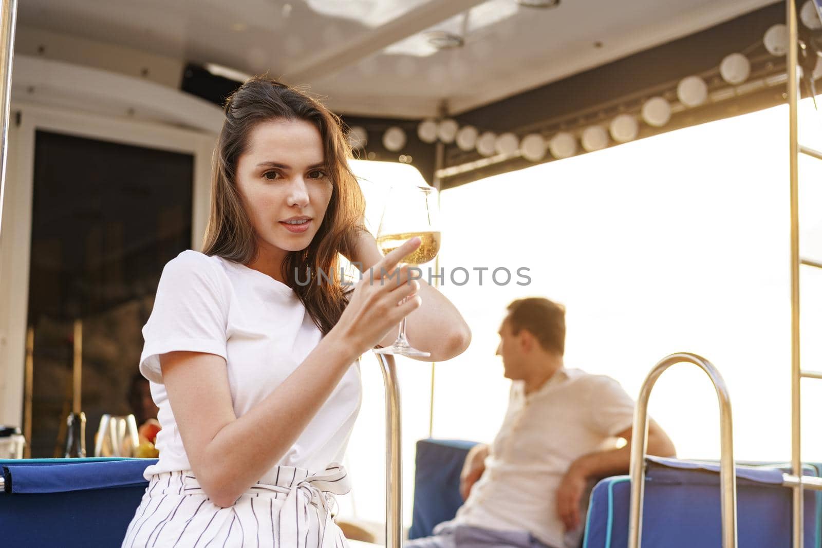 Young woman holding a wineglass and sitting on deck of sailing yacht boat