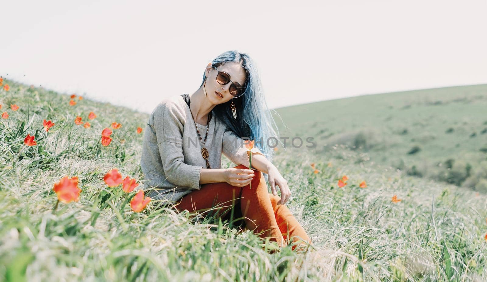 Beautiful young woman in sunglasses rests on red tulip meadow, looking at camera.