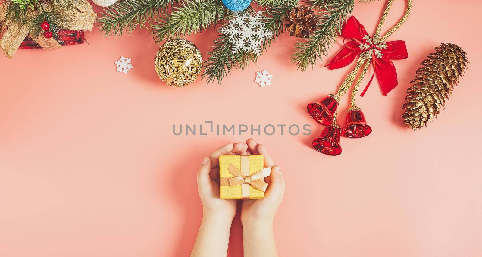 The child is holding a New Year's gift on a pink background with New Year's decorations.