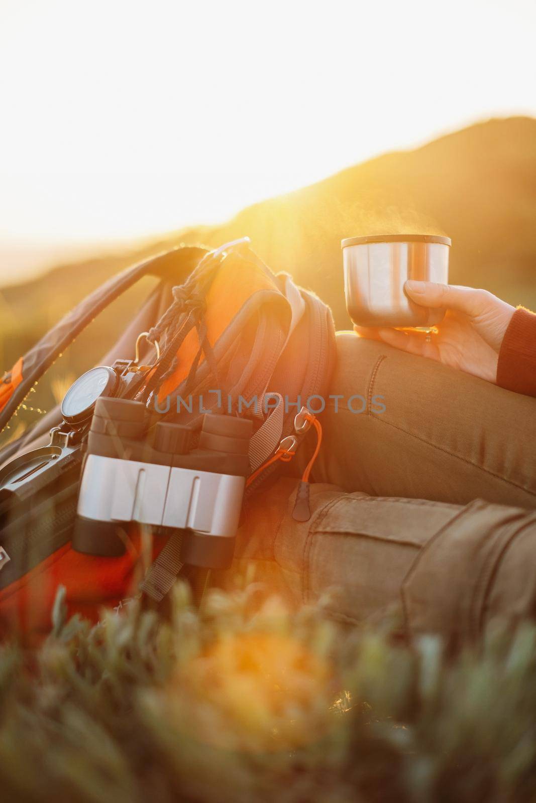 Unrecognizable hiker young woman rests with tea in summer mountains at sunset.