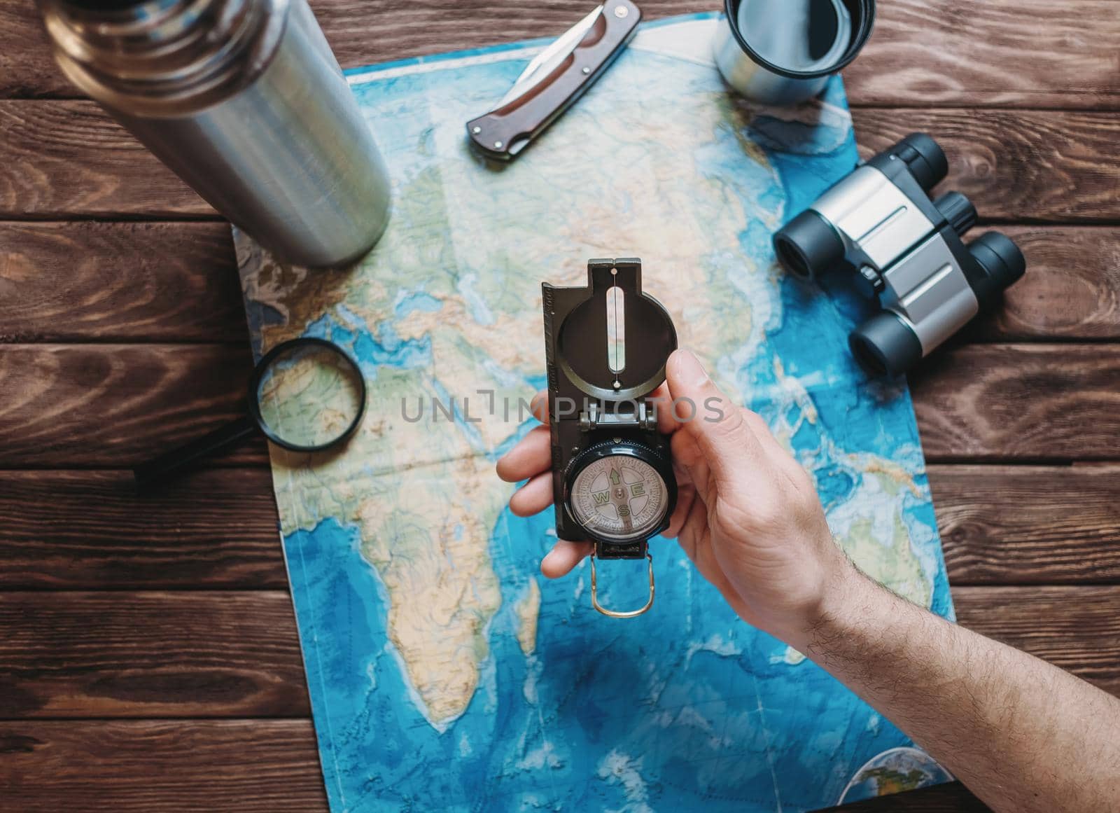 Man holding a compass over a map and planning to travel, point of view. Focus on the compass. The map is blurred