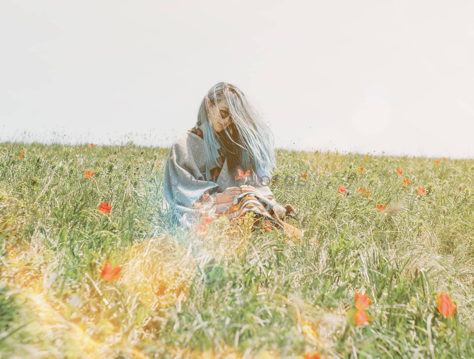 Beautiful young woman with blue hair rests on red tulips meadow on sunny day.