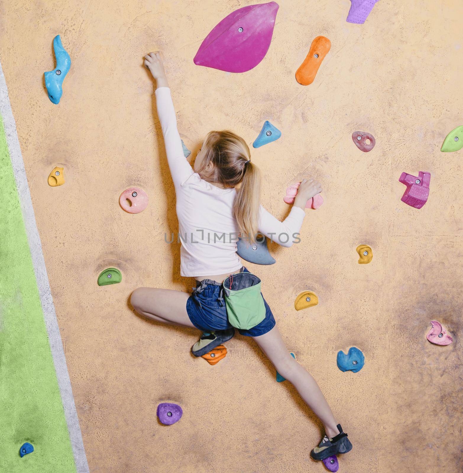 Little girl free climbing on artificial wall in gym, bouldering.