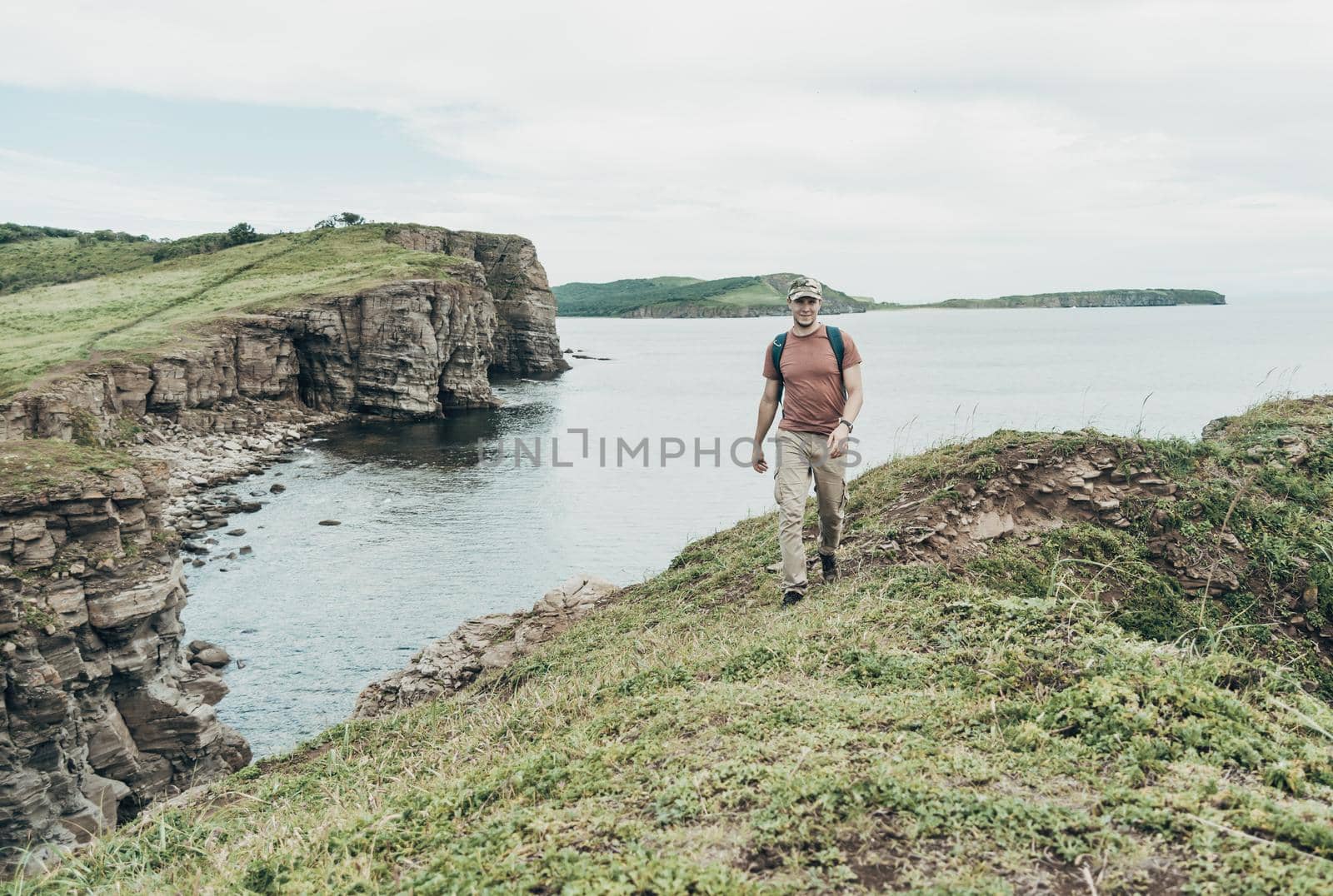Traveler young man walking on high coastline on background of sea.