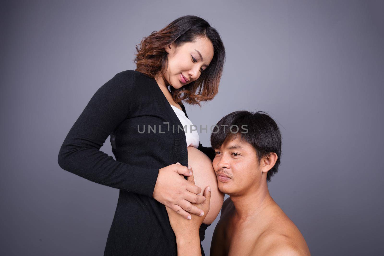 young couple: pregnant mother and happy father on gray wall background