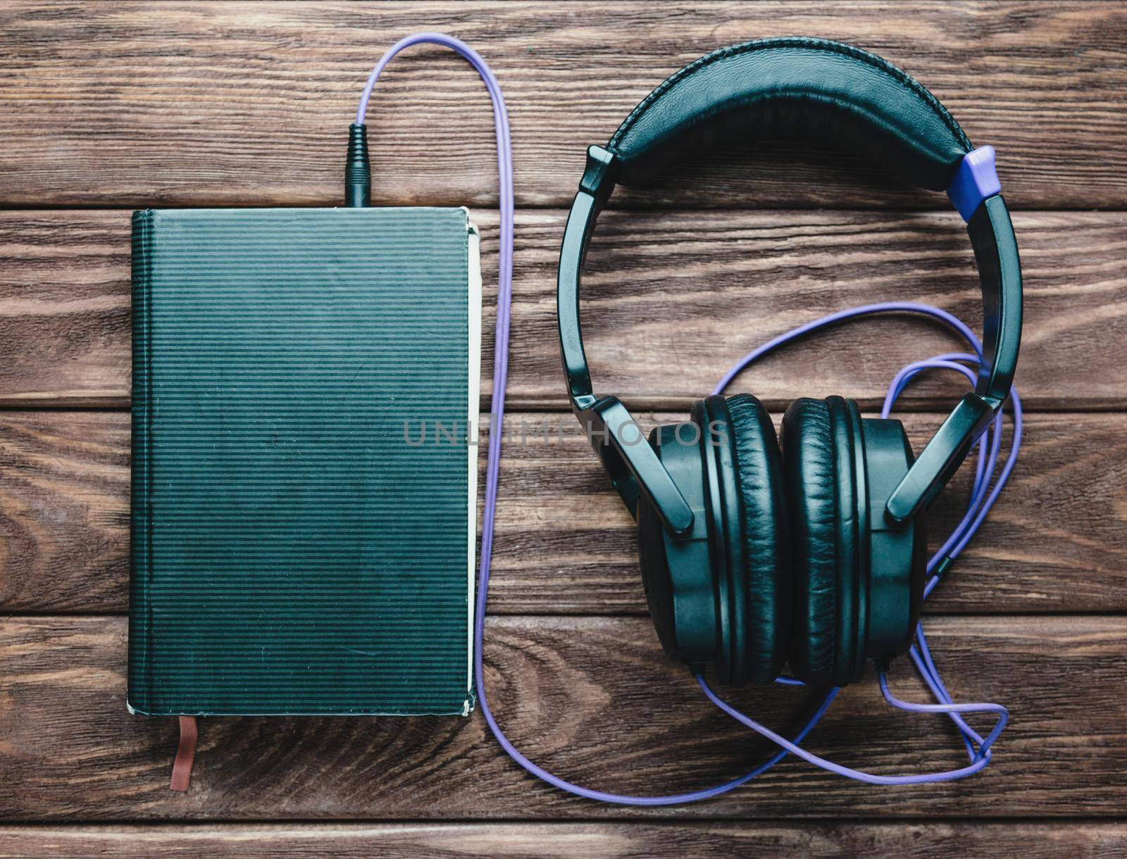 Headphones with a book on a wooden background, top view. Concept of audiobook.