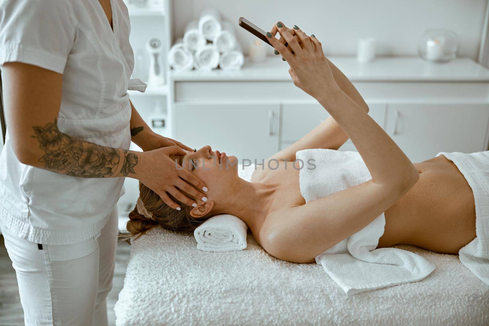 Therapist is doing face relaxing massage to a young woman in modern wellness cabinet