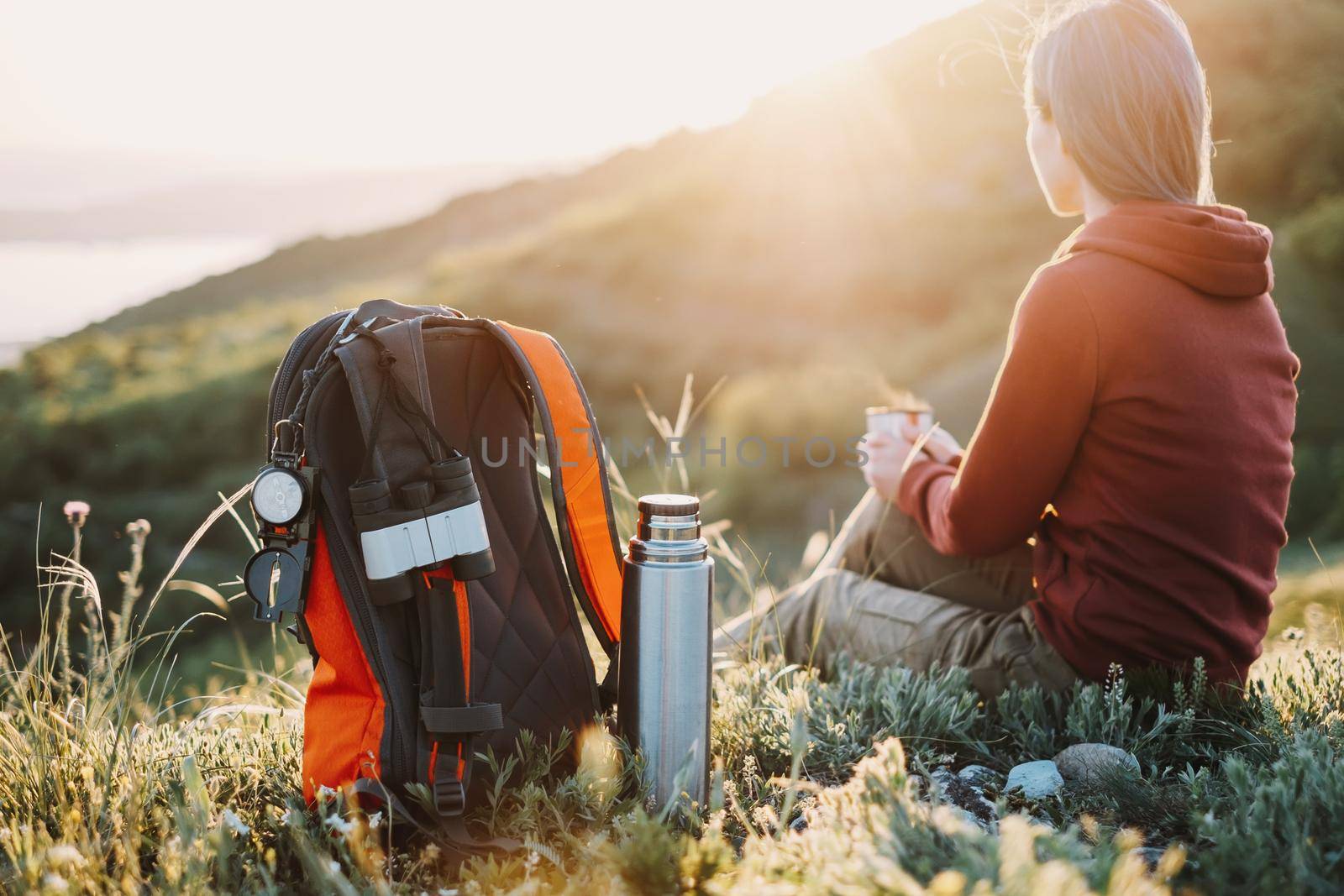 Hiker young woman with backpack rests in summer mountains at sunset.