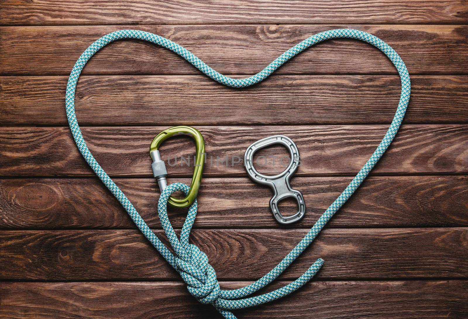 Climbing rope in the shape of a heart with carbine on wooden background, top view.