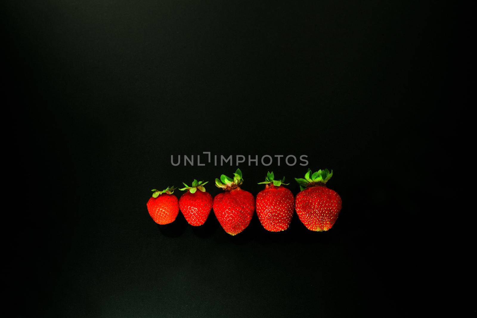 red strawbery on black background. red strawwberies ina line