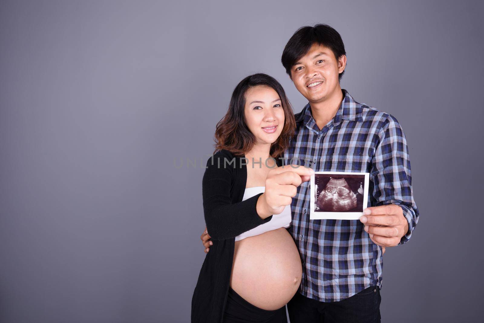 happy pregnant and husband showing ultrasound image on gray wall background