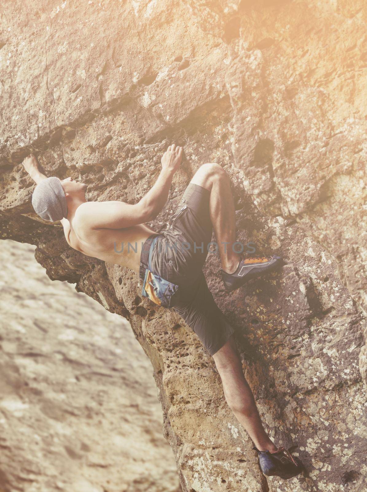 Strong young man free climbing on rock outdoor on sunny day.