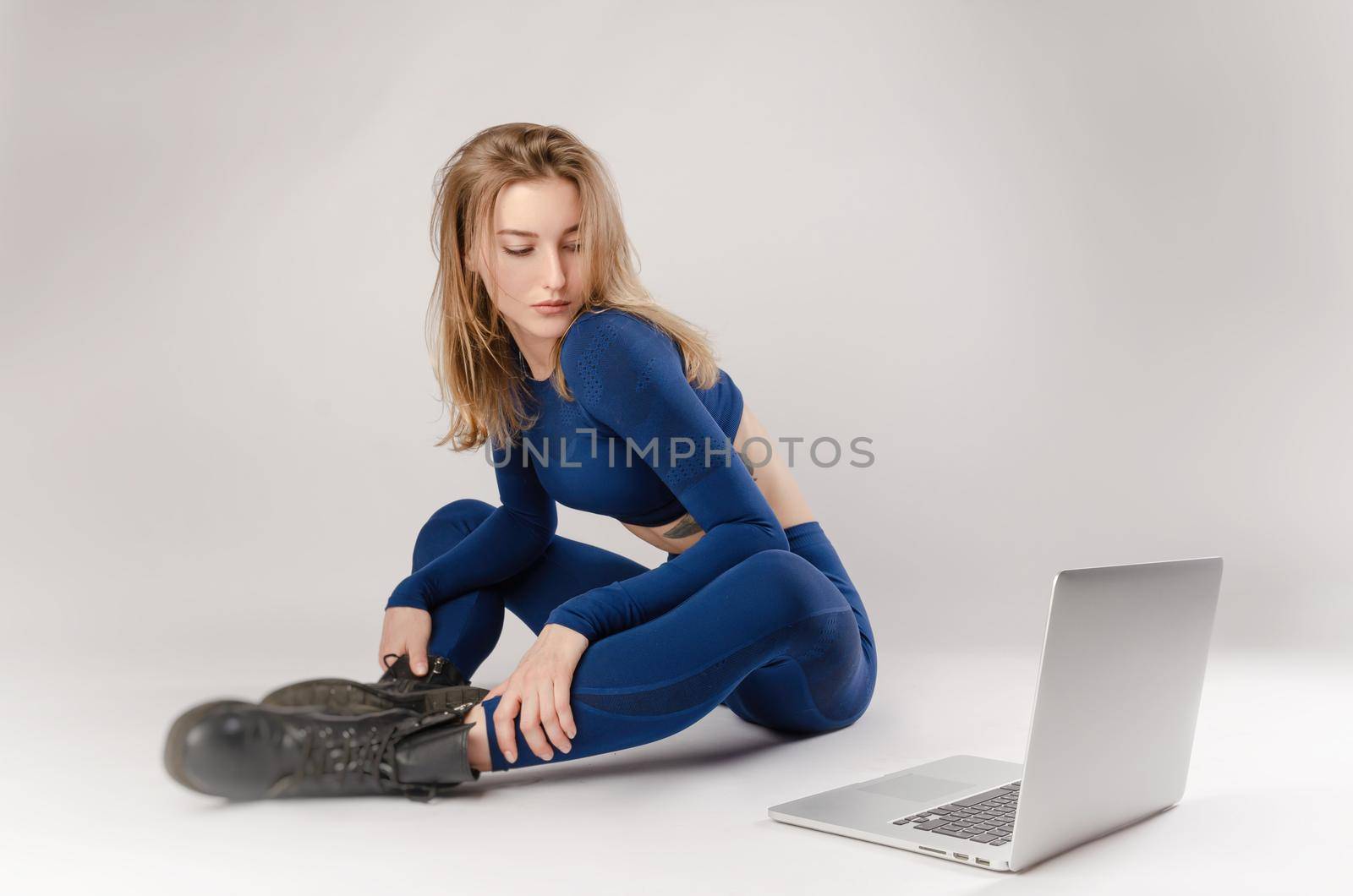 athletic girl posing in the Studio performing exercises online on a laptop on a white background by Rotozey