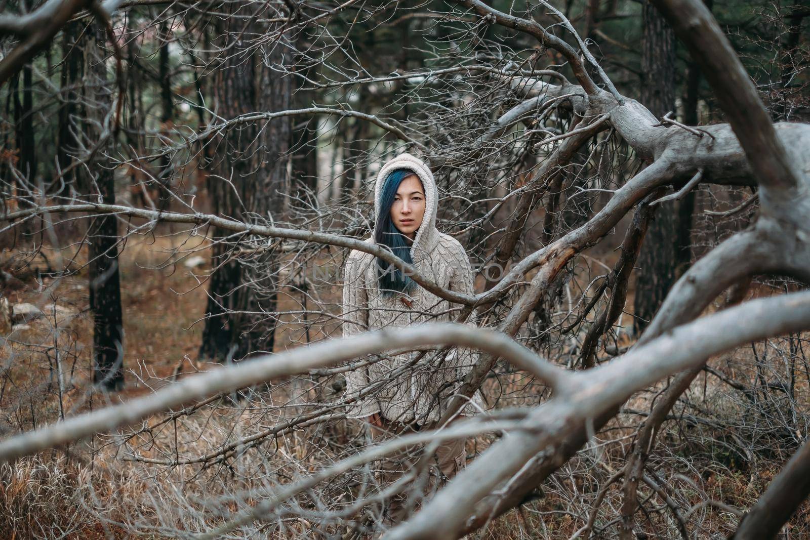 Sad lonely young woman walks in the woods among dry trees without leaves.
