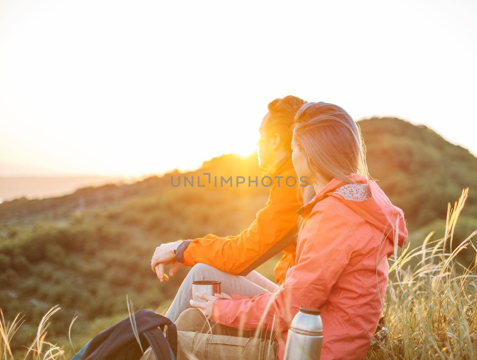 Traveler young couple resting in summer mountains at sunset and enjoying view of nature.