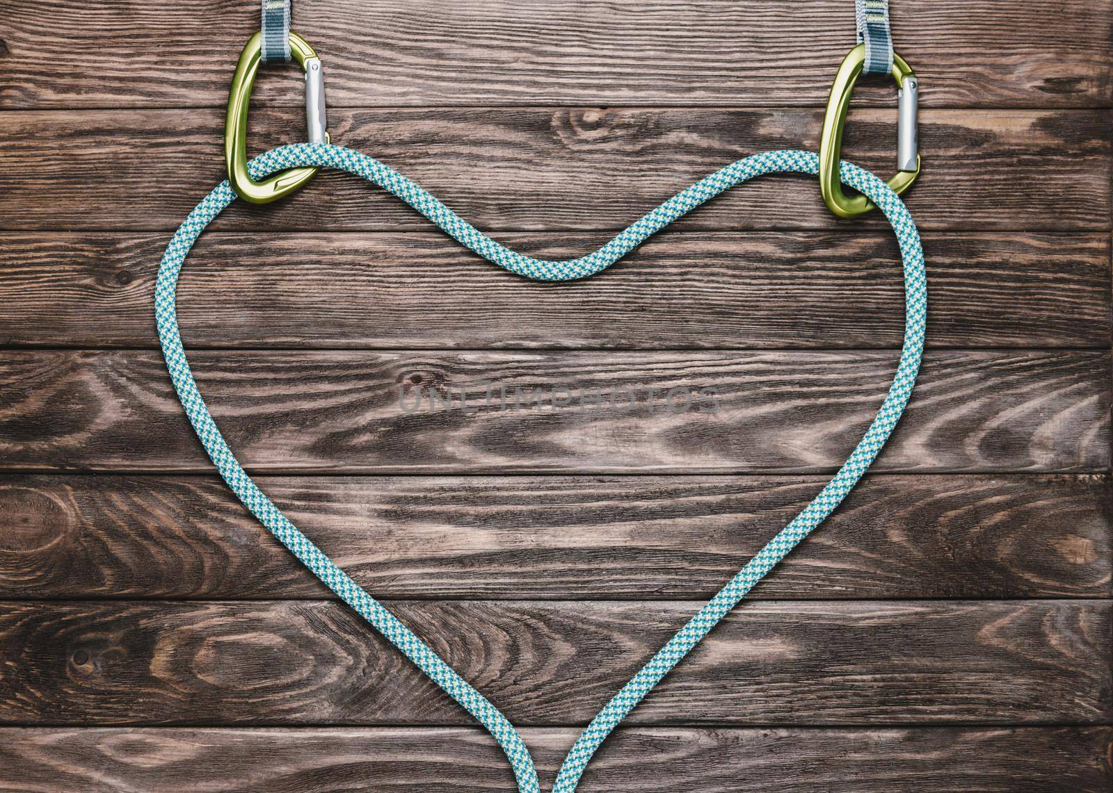 Rope for climbing sport in shape of a heart with carbines on wooden background, top view. Copy-space.