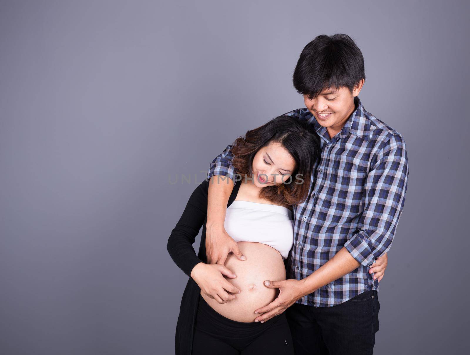 young couple: pregnant mother and happy father on gray wall background