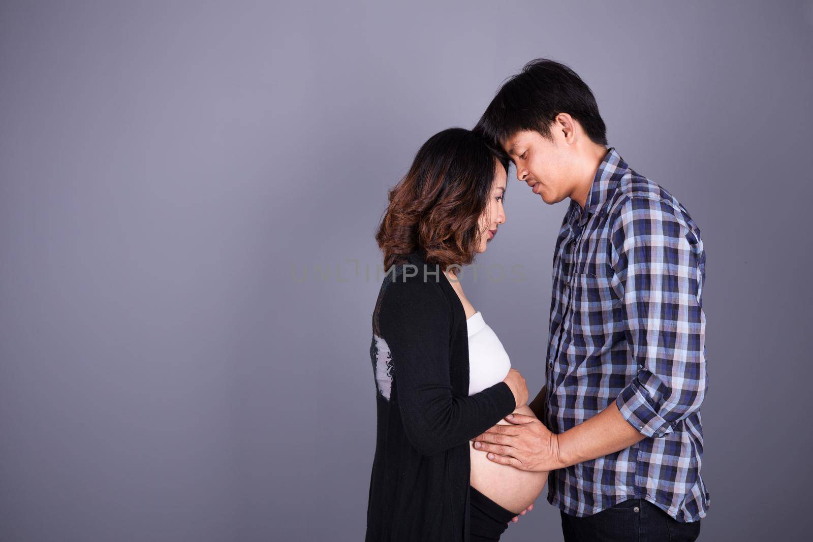 young couple: pregnant mother and happy father on gray wall background