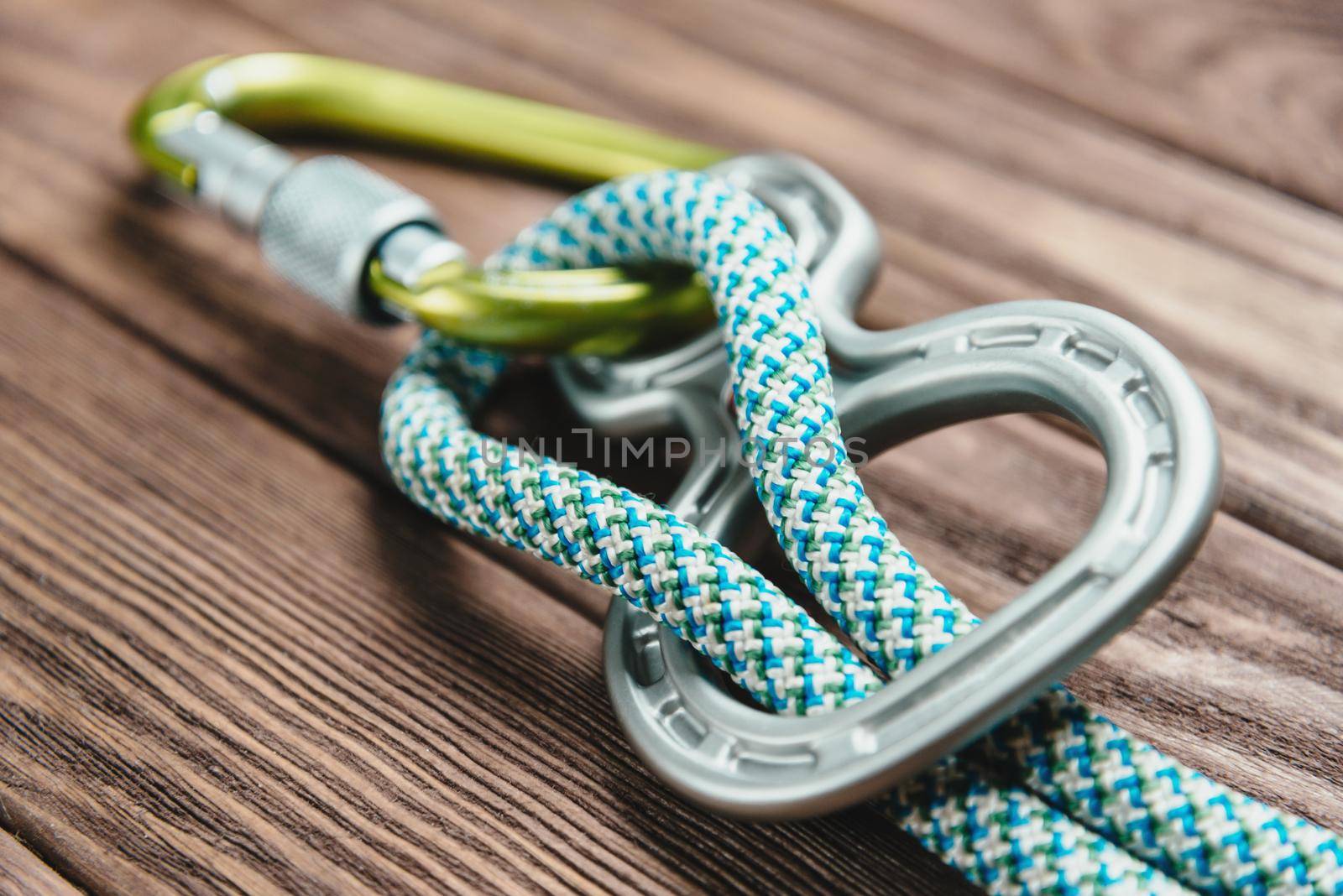 Climbing belay device with rope and carbine on wooden background.