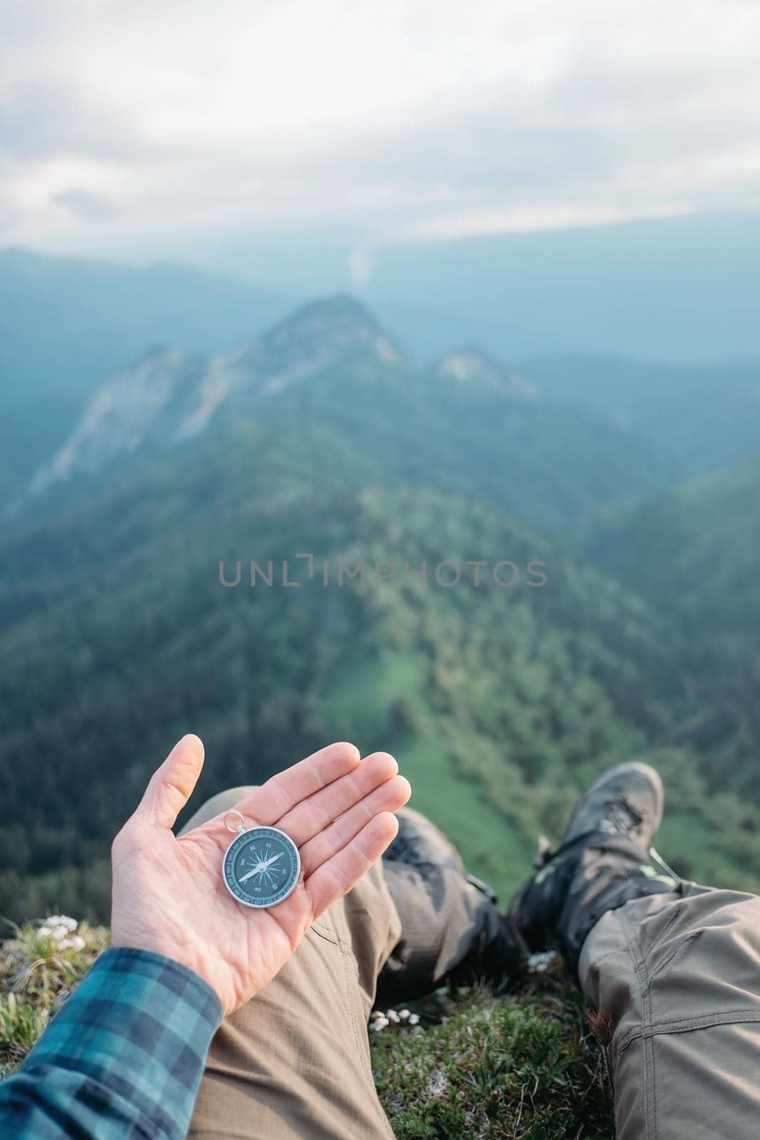 Hiker young man with compass sitting in summer mountains and searching direction, point of view.
