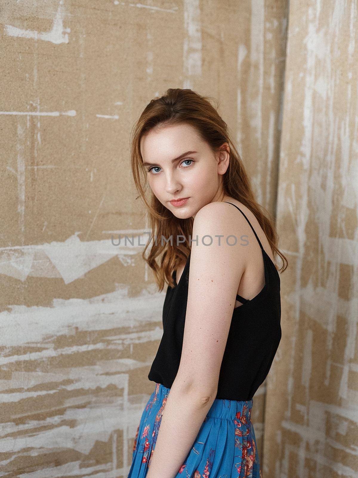 Beautiful young woman in black top, blue skirt, indoors portrait of cute thoughtful model. caucasian skinny female with long brown hair on abstract background. natural pretty lady posing at studio
