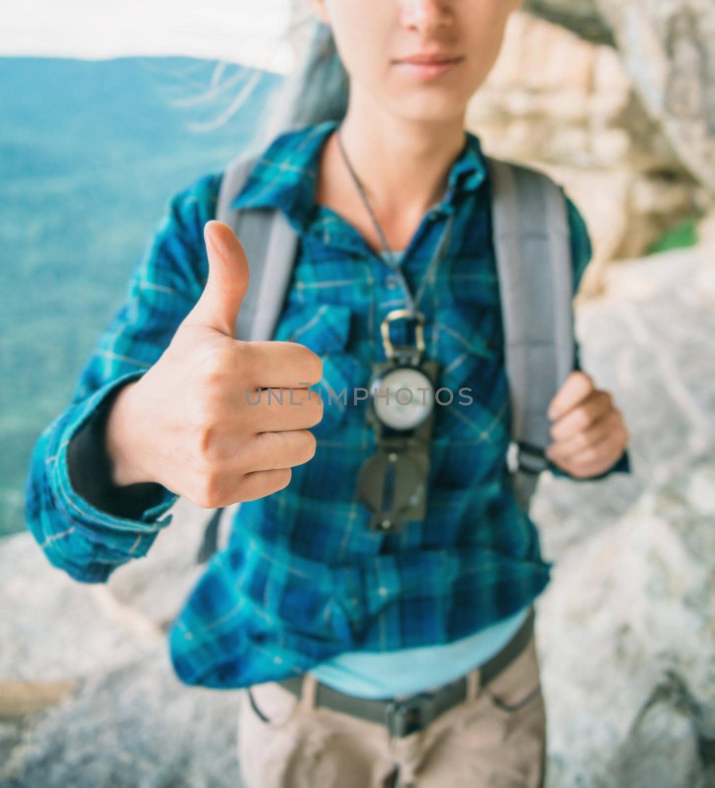 Backpacker young woman with compass showing thumb up gesture outdoor.