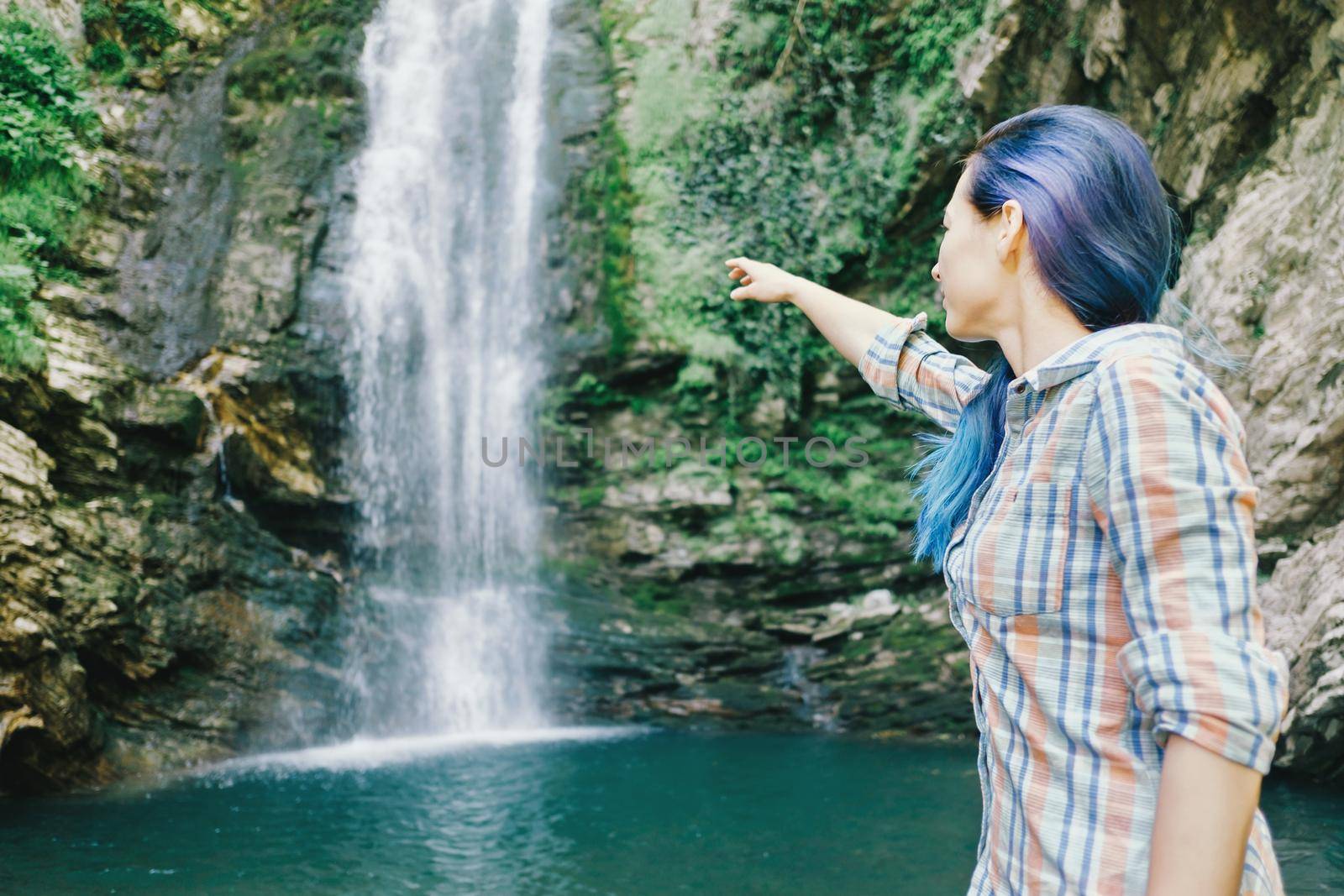 Explorer young woman pointing at waterfall in summer.